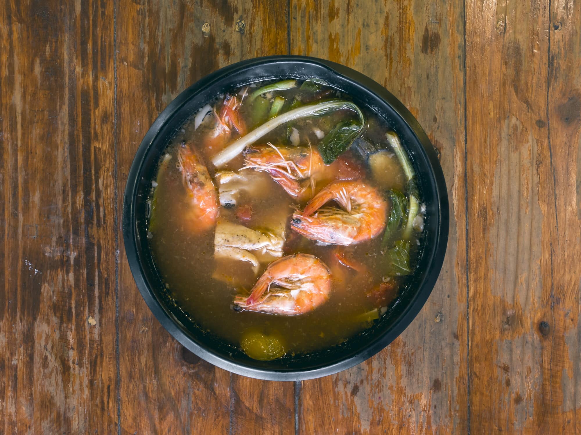 Sinigang na Hipon is a type of Filipino sour tamarind soup. Top view, on a wood table.