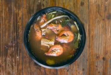 Sinigang na Hipon is a type of Filipino sour tamarind soup. Top view, on a wood table.