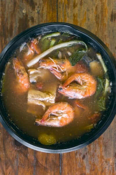 Sinigang na Hipon is a type of Filipino sour tamarind soup. Top view, on a wood table.