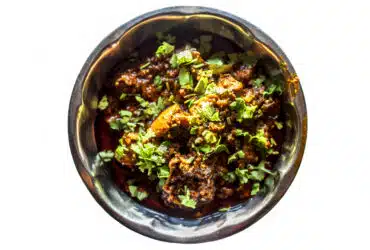 Top shot of achari chiken in serving plate isolated on white background.