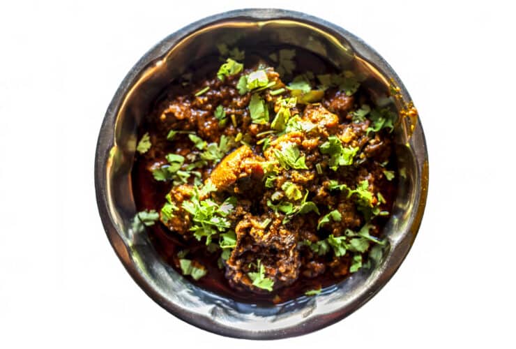 Top shot of achari chiken in serving plate isolated on white background.