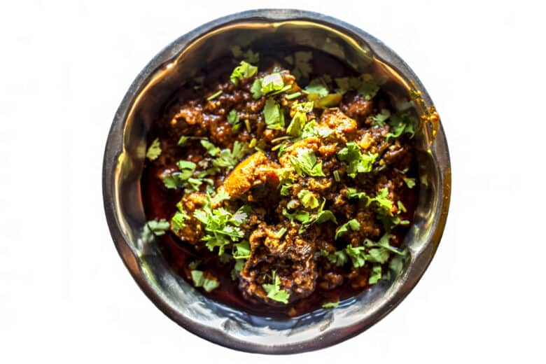 Top shot of achari chiken in serving plate isolated on white background.