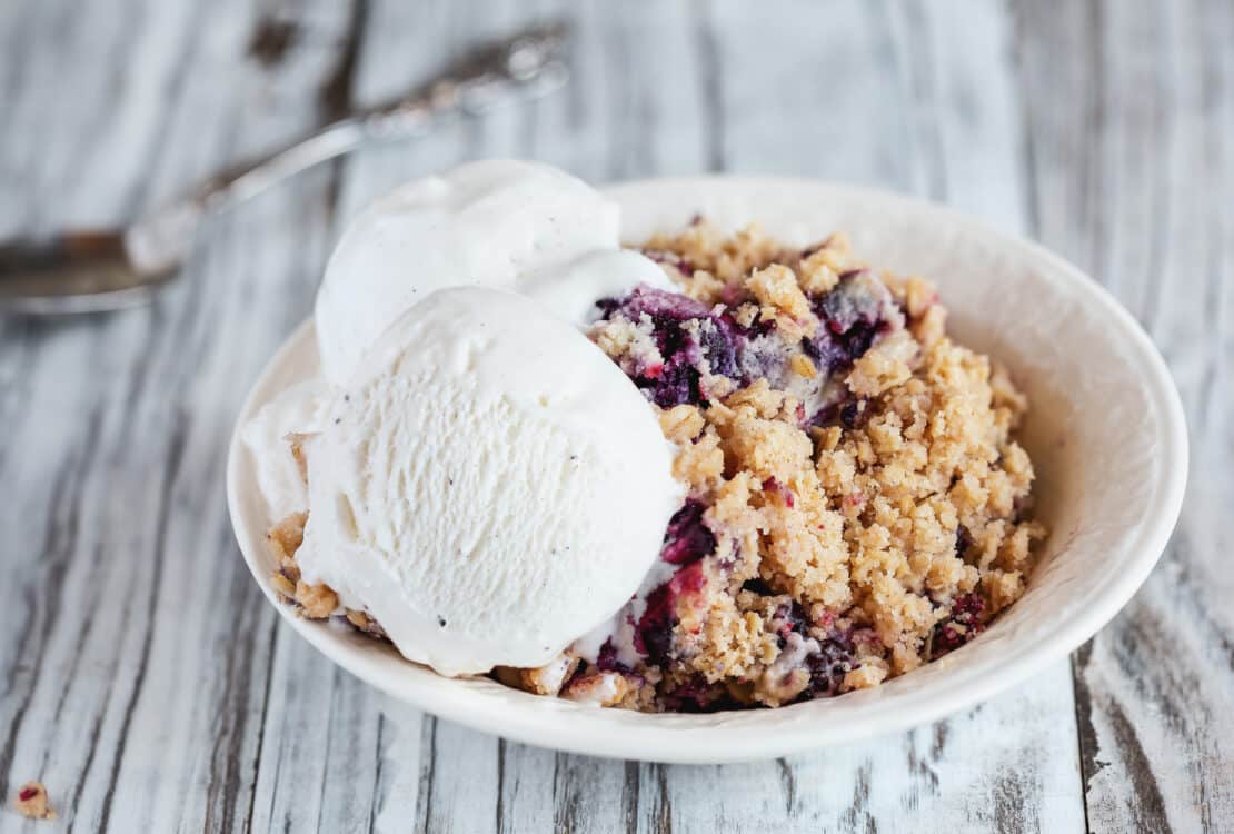 Blackberry and Blueberry Cobbler topped with a golden oatmeal crisp with ice cream. Extreme selective focus with blurred background.