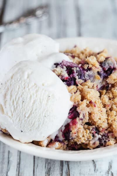 Blackberry and Blueberry Cobbler topped with a golden oatmeal crisp with ice cream. Extreme selective focus with blurred background.