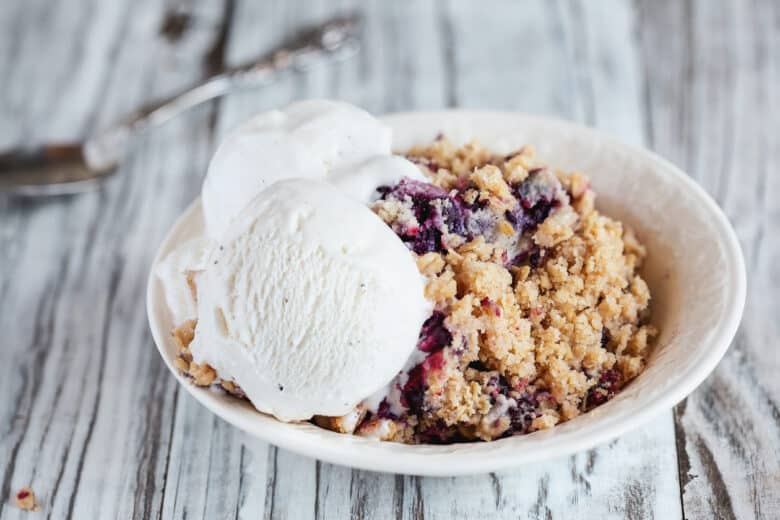 Blackberry and Blueberry Cobbler topped with a golden oatmeal crisp with ice cream. Extreme selective focus with blurred background.