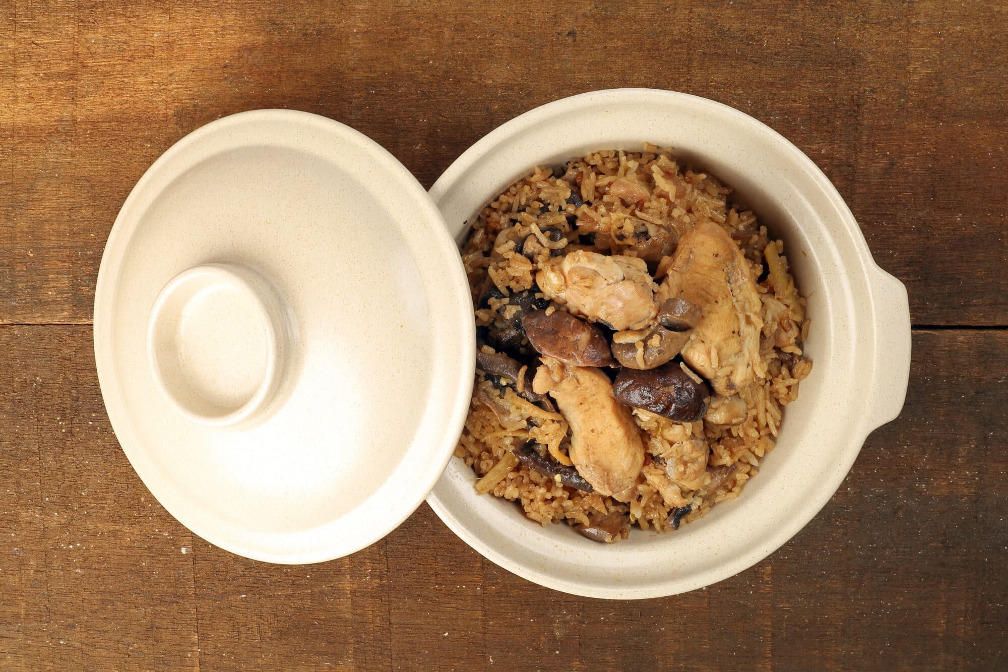 Clay pot chicken rice with mushroom in clay ceramic bowl on rustic wood table background